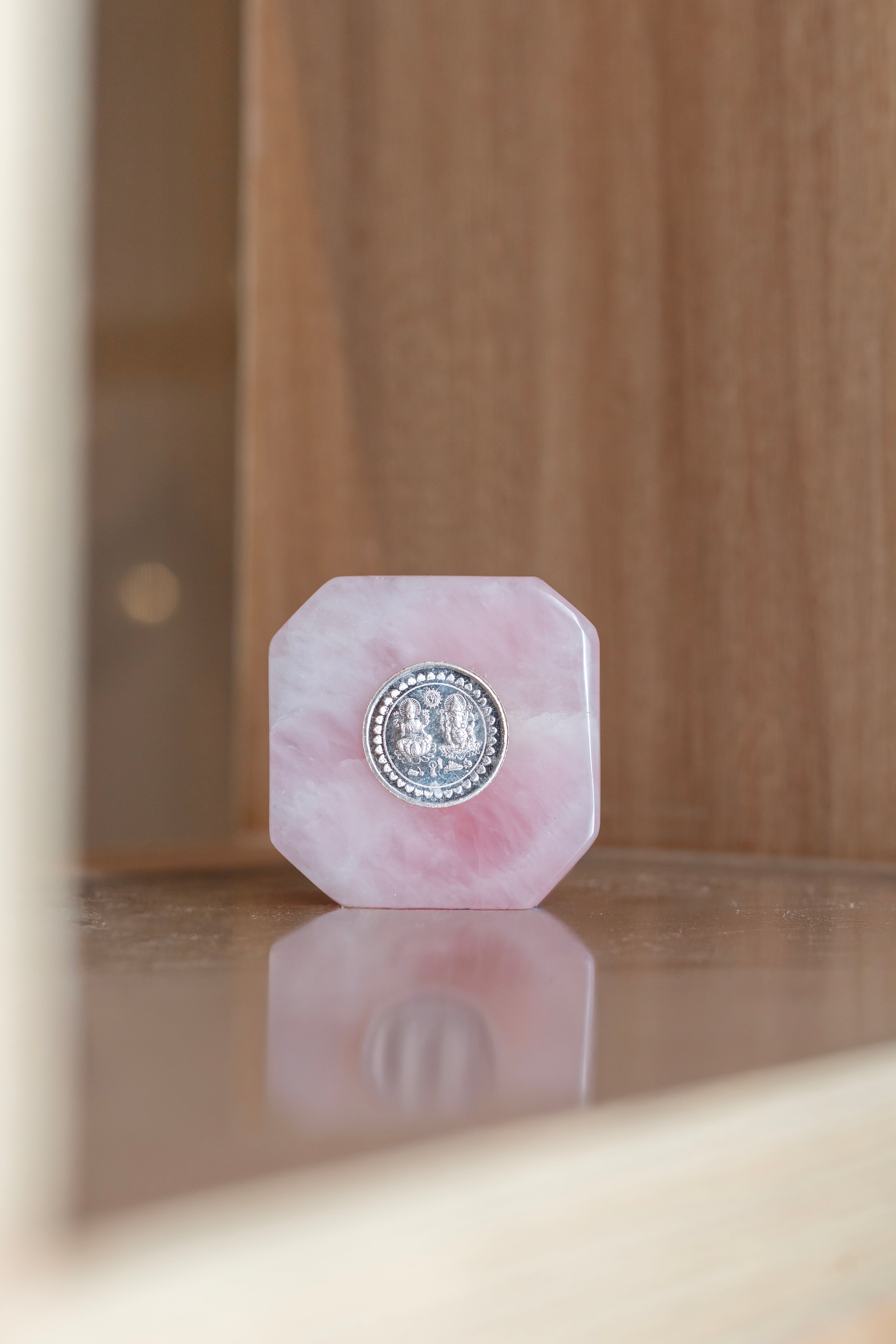 Natural rose quartz crystal base with embedded silver coin, crafted by Rasava Jewels, showcasing a smooth, polished gemstone with metallic accents.