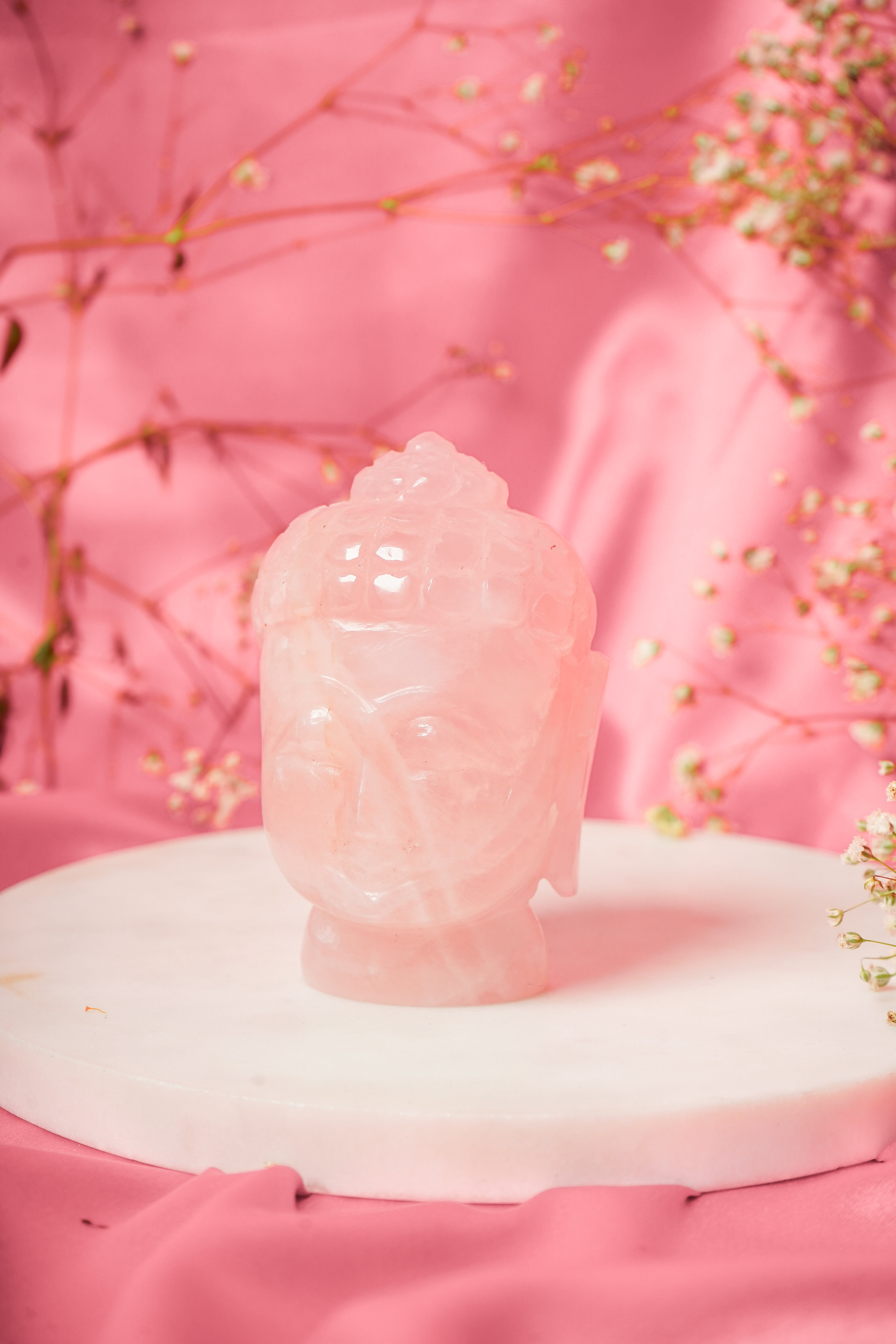 Natural rose quartz Buddha head sculpture with smooth polished surface and serene facial expression.