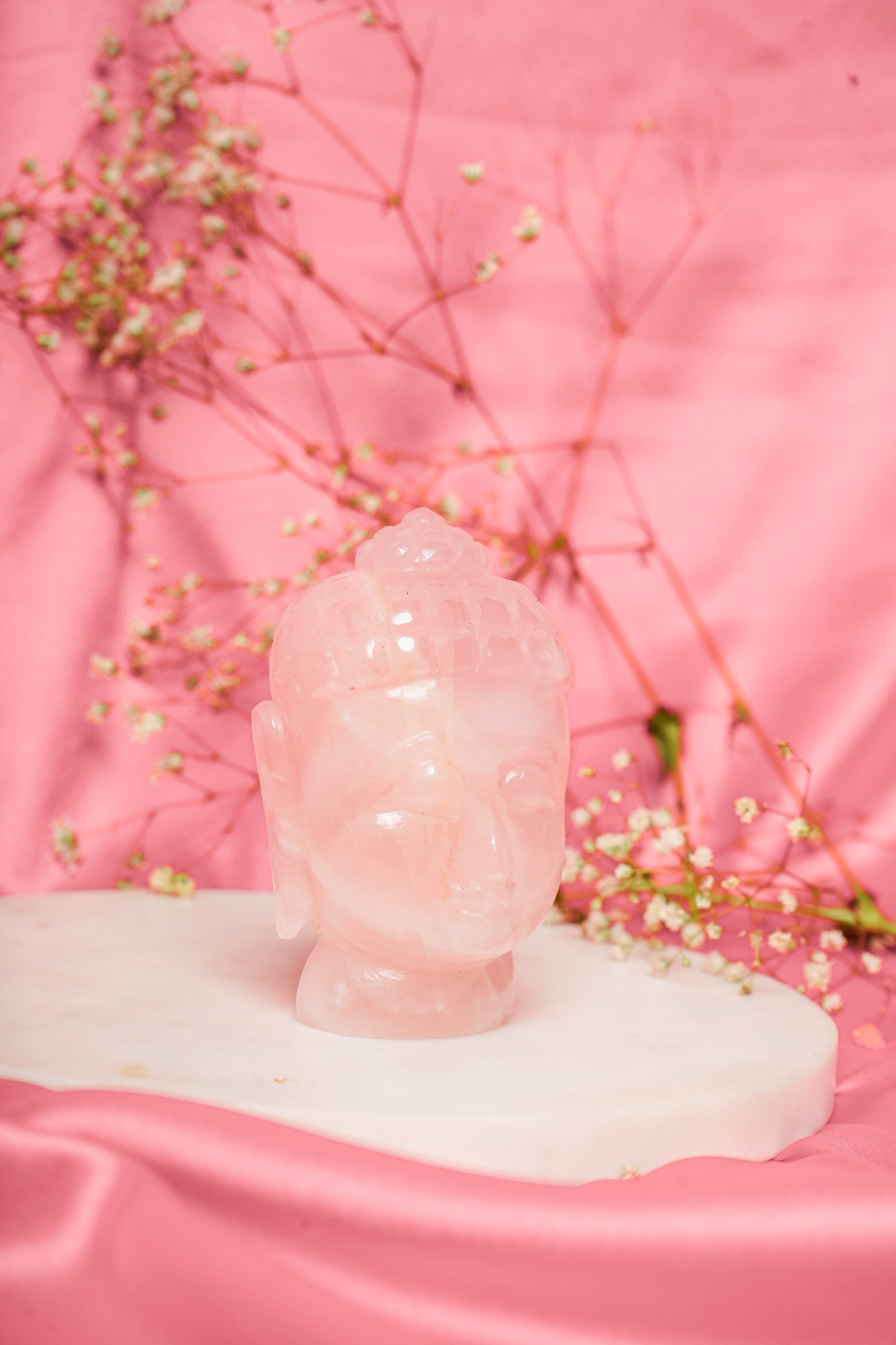 Natural rose quartz Buddha head sculpture with serene facial features, showcasing soft pink crystal hues and smooth polished surface.