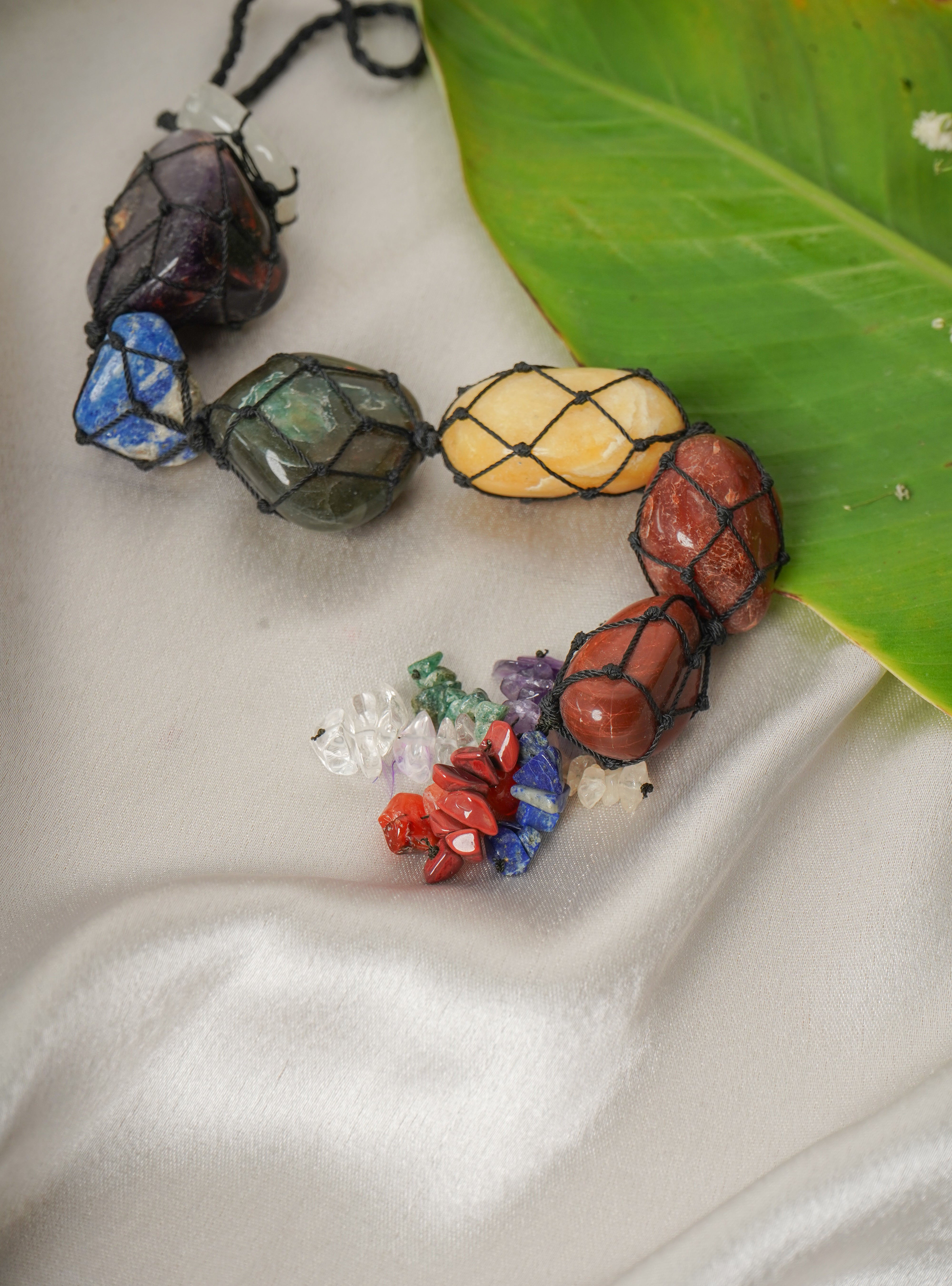 Seven chakra natural stone wall hanging with colorful stones arranged in a circular pattern on a decorative background.