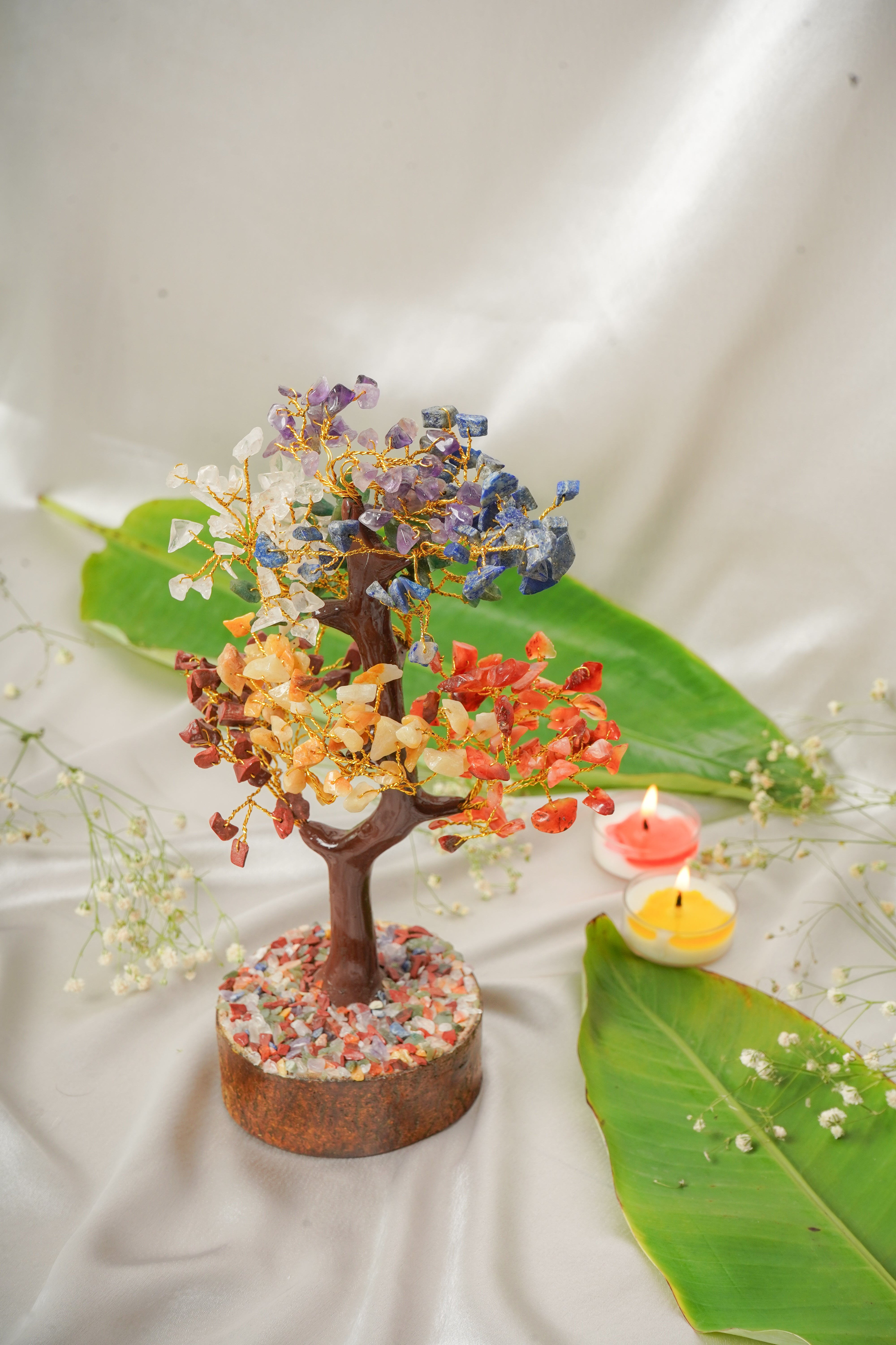 Seven chakra natural stone tree with colorful gemstone leaves arranged on a wooden base, representing balance and harmony.