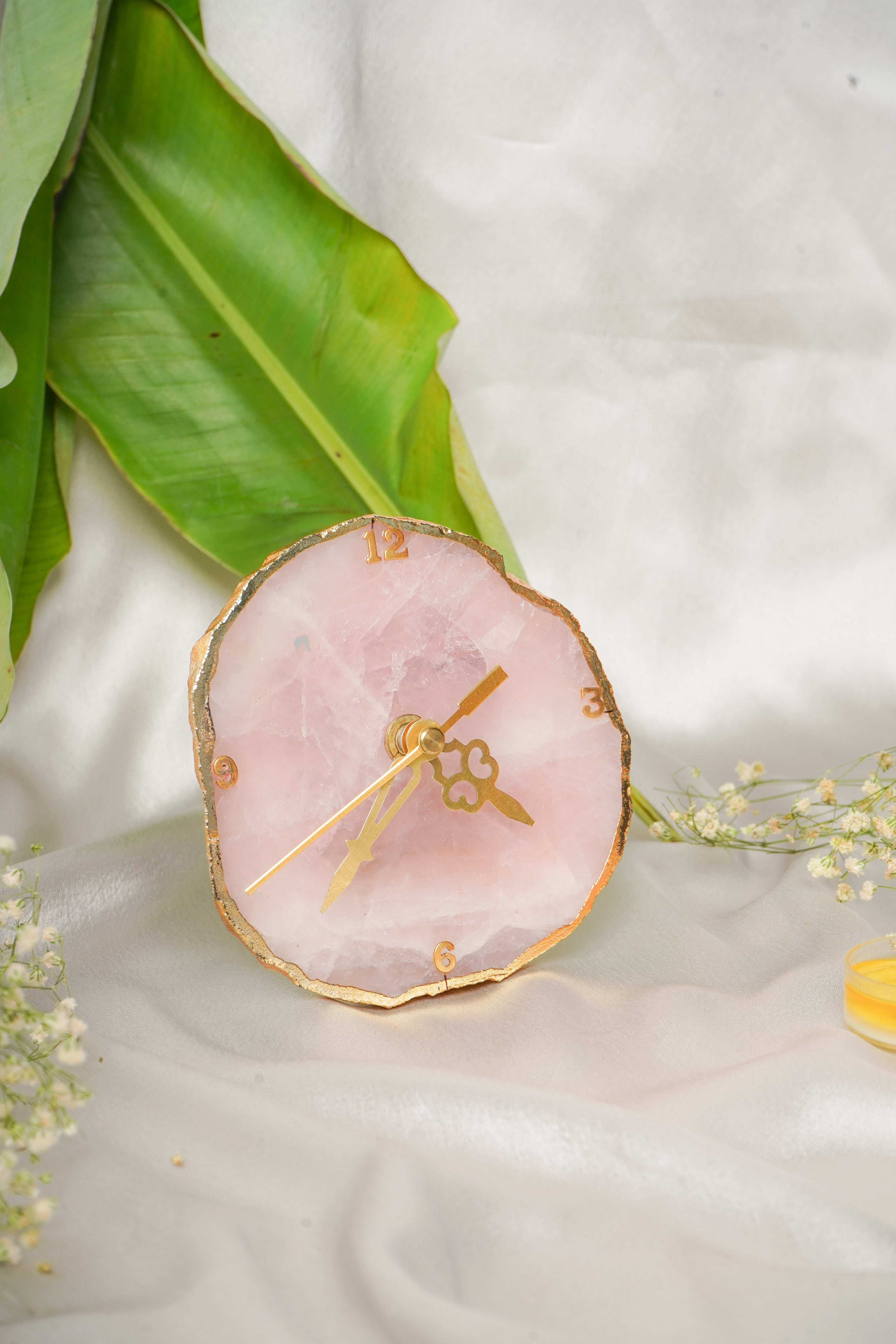 Natural rose quartz table clock with a polished pink crystal base and a round clock face, decorative and elegant home decor piece.