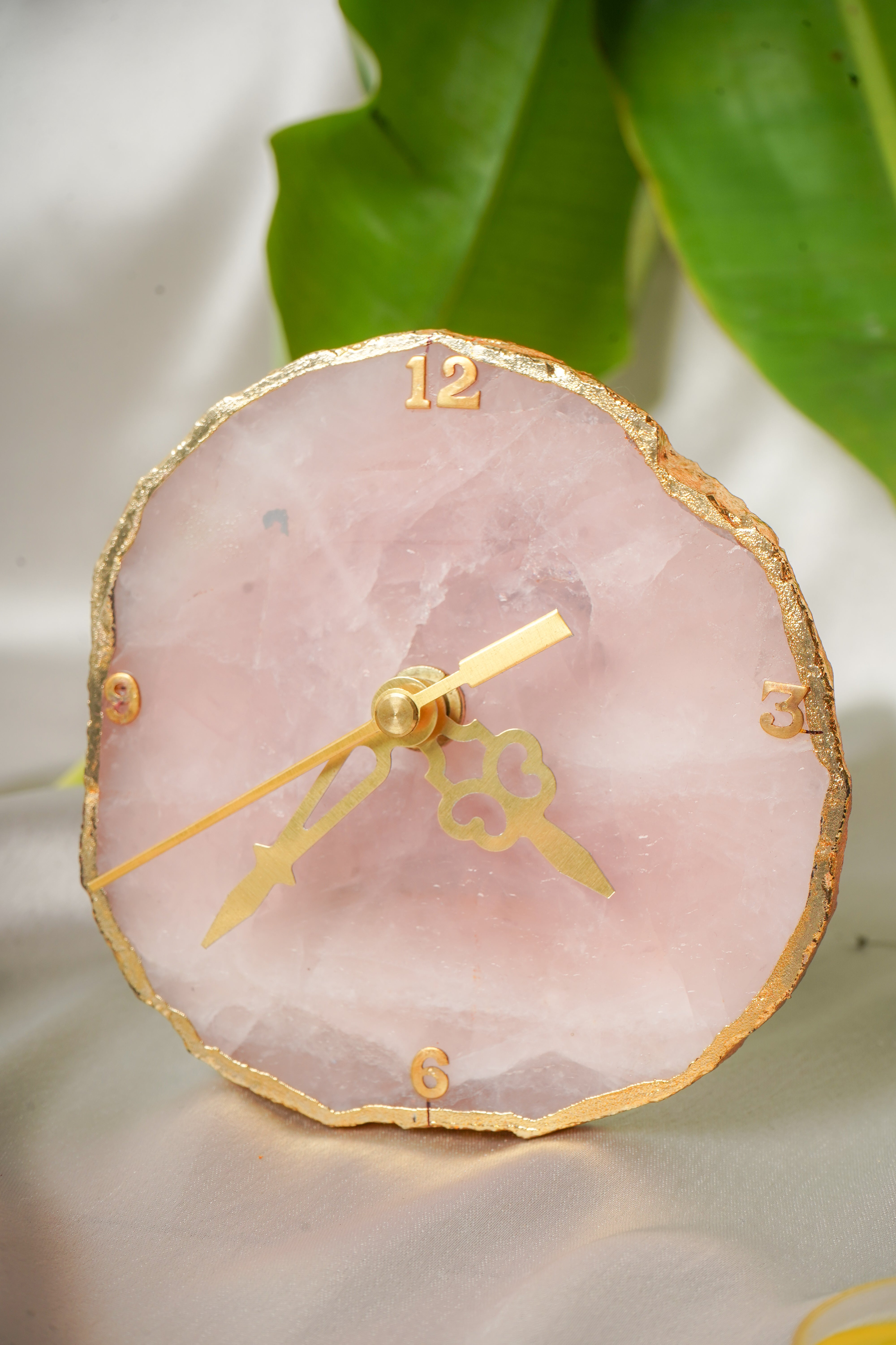 Natural rose quartz table clock with a polished pink gemstone appearance, featuring a round clock face and elegant design.