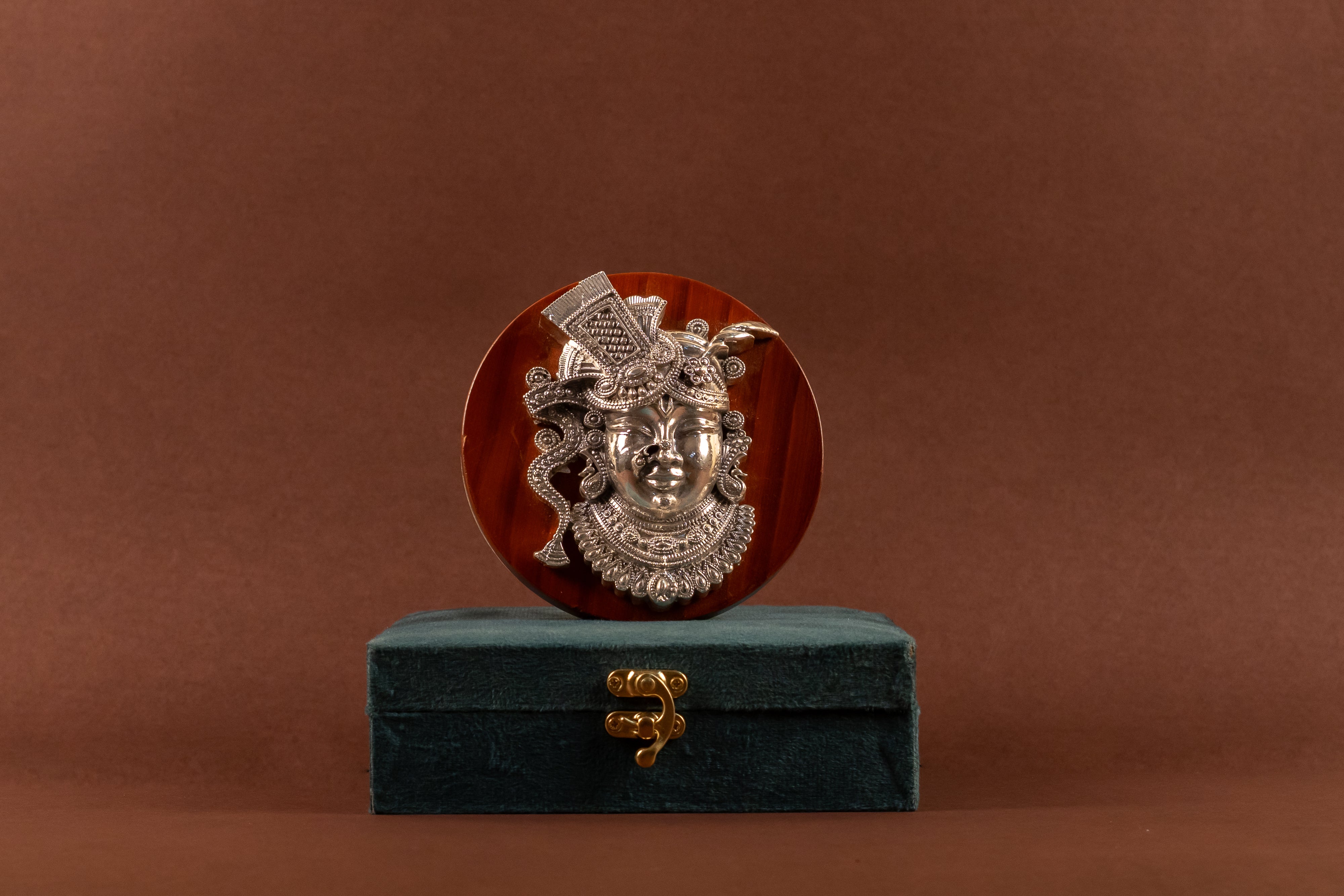 Pure silver Shrinathji idol on wooden frame, detailed craftsmanship, from Rasava Jewels in traditional Indian religious decor.